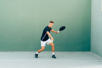 Man playing paddle tennis on an outdoor green paddle tennis court at the sunset