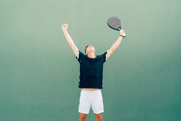 Paddle tennis player celebrating victory at the end of the match on the green court at sunset