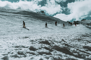 People in winter enjoying the snowy mountains where are practised plenty of activities such as skiing and snowboarding with a clear sky and some clouds on the horizon.