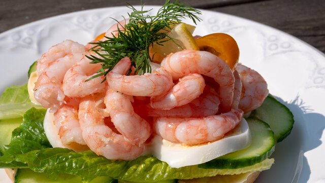 Close up of peeled fresh shrimps on white rye bread, making up a delicious Swedish shrimp sandwich (r&auml;kmacka).
Seafood and food preparation concept.