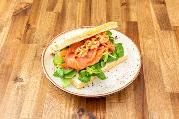 Smoked salmon focaccia with cheese spread on the bread, chopped walnuts and a bed of lamb's lettuce on varnished wooden plate