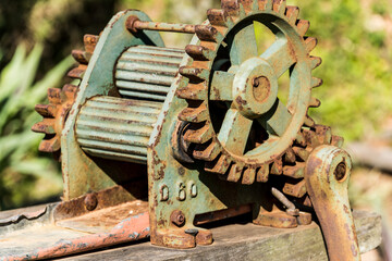 Old green metal cane grinder with some rust. Rustic equipment on top of a piece of wood.