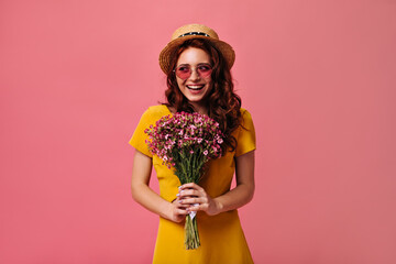 Happy Lady in yellow dress posing with pink bouquet. Charming girl in summer dress and pink glasses holds flowers and smiles