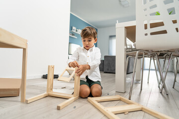 Small caucasian boy four years old playing with self assembly chair or table on the floor at home...