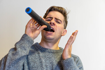 Handsome man with a microphone singing with gray sweater and white background
