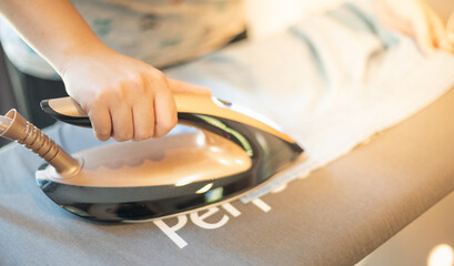 Female hand ironing clothes on iron board at home on the laundry day.