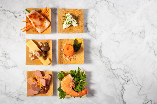 Top view of six delicious appetizers on a small wooden plate on a marble texture table
