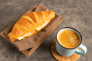 Crunchy delicious croissant with ham and cheese filling and a mug of hot coffee on a table