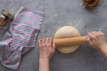 White woman hands rolling a soft bake dough with a wooden rolling pin.