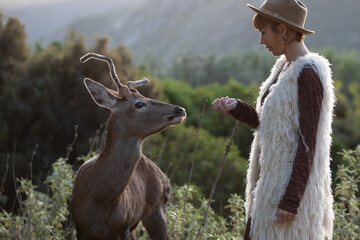 Young beautiful elegant woman with a deer in a forest. Natural wildlife conservation park.