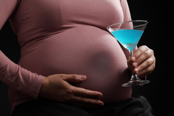 Close up pregnant woman holding blue cocktail in glass on black background