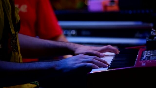 At a concert performance on stage, a close up of a male musician hands playing the red synthesizer keyboard.