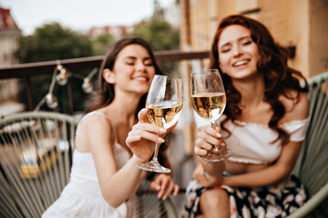 Attractive women enjoy good day with wine on terrace. Lovely girls in great mood have fun and pose for camera