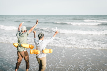 Senior couple take off and throw the face mask while happily running down to the beach. Senior...