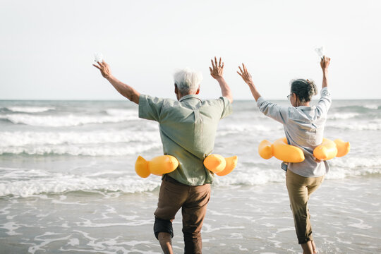 Senior couple take off and throw the face mask while happily running down to the beach. Senior couple show hands with enjoying on the beach, plan life insurance and retirement concept..