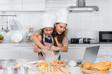 little girl having fun learning baking bakery online in kitchen with mother