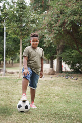 Portrait of cute African American boy with soccer football ball doing exercise in the park