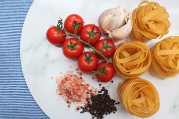Italian Pasta Cooking Ingredients on White Marble Background. Fettucine, tomatoes, salt, pepper, garlic.