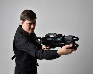 close up portrait of a  brunette man wearing leather jacket  and holding a science fiction gun.  action pose isolated  against a grey studio background.