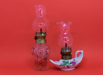 Two antique decorative kerosene lamps, one white and the other glass, isolated on a red background. horizontal close-up