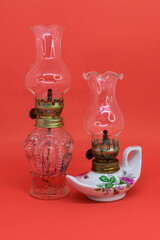 Two antique decorative kerosene lamps, one white and the other glass, isolated on a red background. vertical close-up