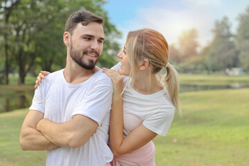 Fototapeta na wymiar young caucasian couple are in love. man and girl wearing white shirt hugging in the park during summer season with smiling and happy face