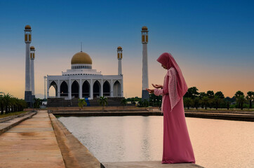 Veiled Islamic muslim woman wearing a burka standing and praying in a beam of overhead light in...