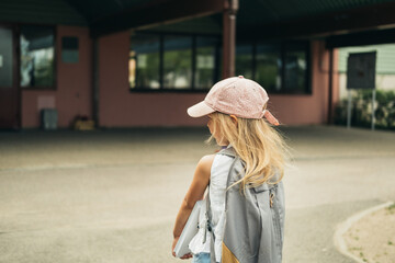 The cute girl, elementary school student, walking to school with bag behind back and book. Students are ready for the new year. Back to school.