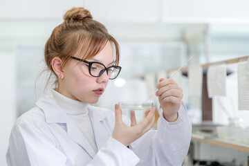 In a chemical laboratory, a girl laboratory assistant puts a chemical into a petri dish with a mini-spatula. Assistant in the chemistry laboratory at the university