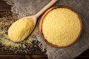 Dry couscous in wooden bowl on dark wooden background.