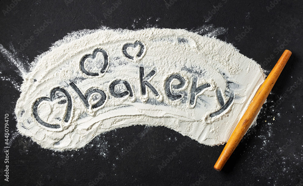 Poster word bakery and heart is written on flour with rolling pin, top view. abstract baking backgroun