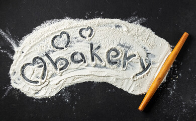 Word bakery and heart is written on flour with rolling pin, top view. Abstract baking backgroun
