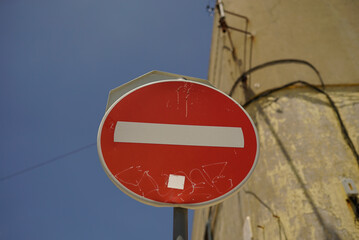 Circular red-white banning signpost against blue sky and building