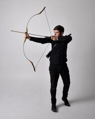 Full length portrait of a  brunette man wearing black shirt and waistcoat holding  a bow and arrow....