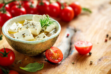 Feta cheese in bowl with olive oil on cutting board with olives, dill and cherry tomatoes, copy space