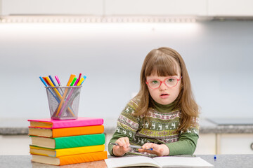 A girl with down syndrome is engaged in creative work at home in the kitchen. Accessibility of education for children with disabilities