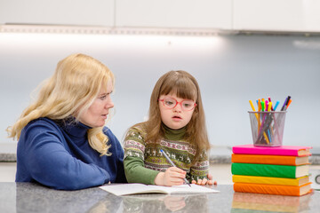 A girl with down syndrome sits next to her mother and is engaged in creativity, drawing a picture in an album. Education for people with disabilities concept