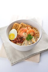 spicy nyonya noodle laksa soup with seafood prawn, fish cake, egg, bean curd and chilli sambal sauce in white background asian halal menu