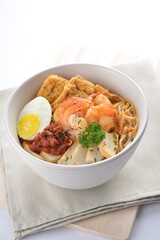 spicy nyonya noodle laksa soup with seafood prawn, fish cake, egg, bean curd and chilli sambal sauce in white background asian halal menu