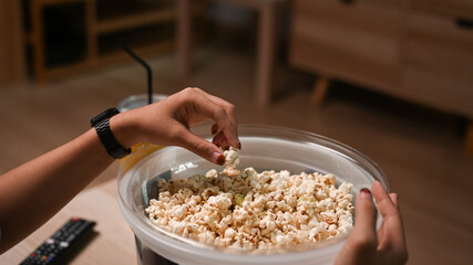 Casual female watching TV and eating popcorn at home.