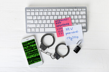 Mobile phone with computer keyboard, handcuffs and papers with passwords on table of hacker