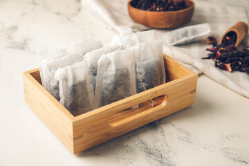 Box of tea bags with dry leaves on light background