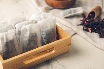Box of tea bags with dry leaves on light background