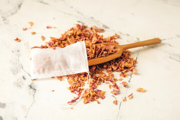 Tea bag and scoop with dry leaves on light background
