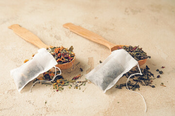 Tea bags and spoons with dry leaves on light background