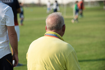 Fathers watching their sons playing football in a school tournament on a sideline with a sunny day. Sport, outdoor active, lifestyle, happy family and soccer mom and soccer dad concepts.