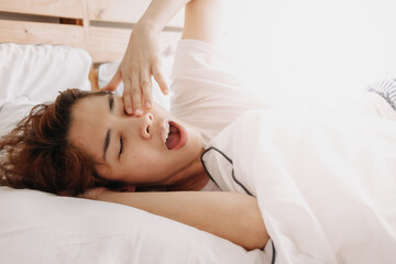 Fototapeta na wymiar Funny sleepy yawning Asian woman just wake up on her bed.