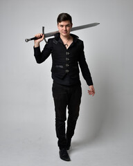 Full length portrait of a  brunette man wearing black shirt and gothic waistcoat holding sword. ...