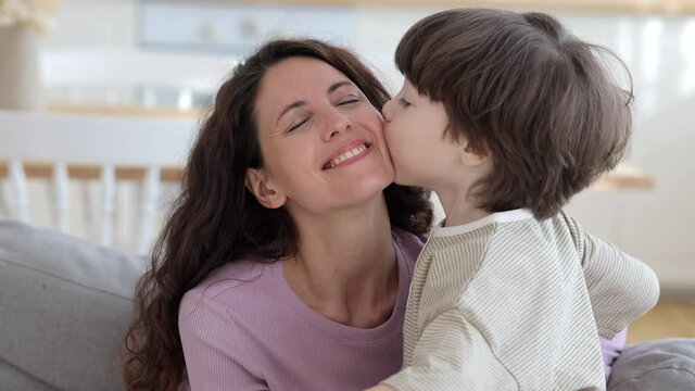 Cute boy of five kissing overjoyed smiling mommy congratulating mom with mother day. Cute little kid embracing young mum. Closeup of happy loving family of two person together at home tender cuddling