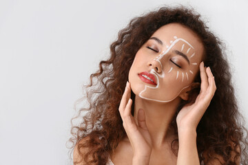 Beautiful young African-American woman with paint on her face against light background